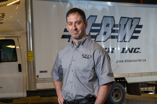 MBW working standing in warehouse in front of delivery truck.